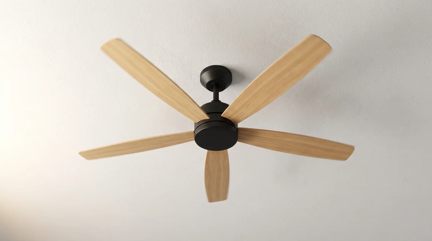 Low angle view of a modern wooden ceiling fan spinning in a room with soft morning light.