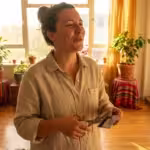A woman working happily on her laptop in a bright, sunlit modern living room, representing financial freedom.